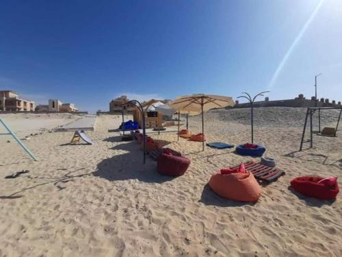 a sandy beach with swings and umbrellas at Seaview luxury Villa in Ras El Hekhma - North Coast in Ras Elhekma