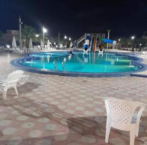 a swimming pool at night with two white chairs at Seaview luxury Villa in Ras El Hekhma - North Coast in Ras Elhekma