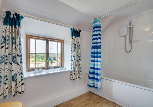 a bathroom with a shower and a tub and a window at Waterside Cottage Westleigh in Westleigh