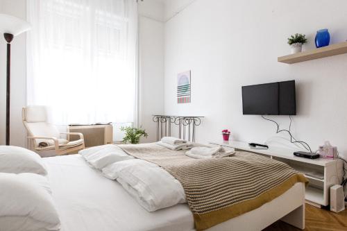 een witte slaapkamer met een bed en een tv aan de muur bij Home in the living Budapest in Boedapest