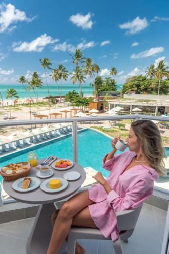 a woman sitting at a table with breakfast on the balcony of a resort at Maragogi Brisa Exclusive Resort in Maragogi