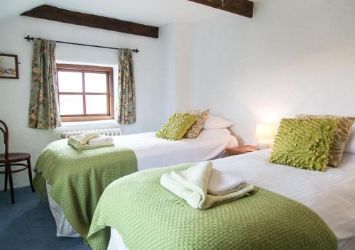 a room with two beds with green sheets and a window at The Granary in Porthcurno