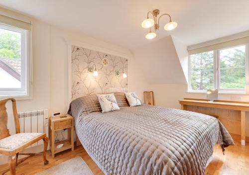 a bedroom with a bed and a chair and two windows at Wisteria Cottage in Parkham