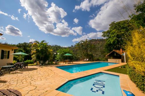 a swimming pool with chairs and a table and a house at Hotel Solar Fazenda Do Cedro in Itaipava