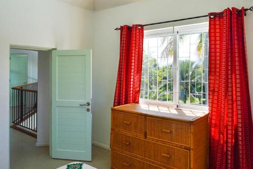 Una habitación con una ventana con cortinas rojas y una cómoda de madera. en Charming villa near Mahebourg with a private pool, en Mahébourg