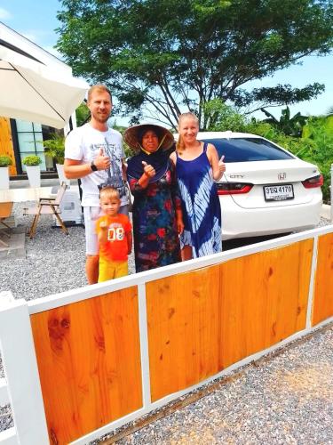 a family posing for a picture in front of a fence at Cana Garden House 1 โฮมสเตย์ in Ban Khok