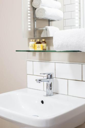 a white bathroom with a sink and towels at The Cricketers Inn in Petersfield