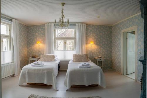 a bedroom with two beds with white sheets and a chandelier at Villa Moisio - puutaloidylliä Salon keskustassa in Salo