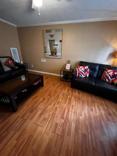 a living room with a black leather couch and wood floors at #2BR Cozy Villa - Mins to Historic STM Amusement Park! in Stone Mountain