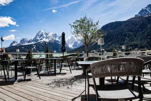 a deck with tables and chairs with mountains in the background at Hotel Gruber in Sesto
