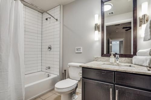 a bathroom with a toilet and a sink and a tub at Stunning 2BR CozySuites with roof pool, lounge gym in Dallas