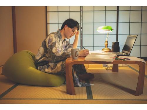 una mujer sentada en el suelo junto a una mesa con un portátil en The Ryokan Tokyo Yugawara - Vacation STAY 21489v en Miyakami