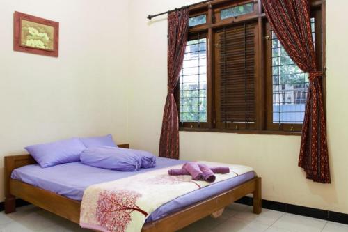 a bedroom with a bed with purple sheets and a window at Joyful Home in Yogyakarta