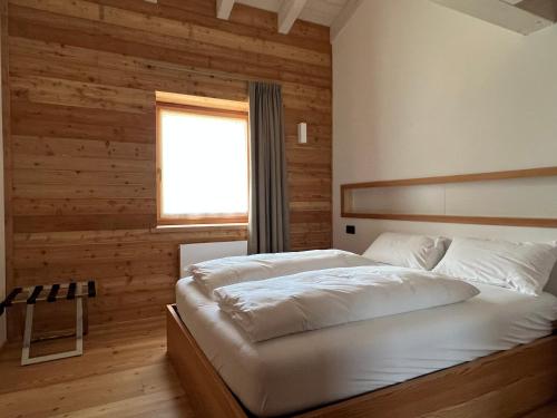 a bedroom with a white bed with a wooden wall at Camelot Luxury Houses Horses in Pellizzano