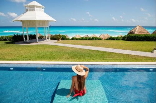 a woman in a hat sitting next to a swimming pool at Paradisus Cancun All Inclusive in Cancún