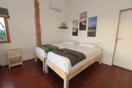 a bedroom with a bed with white sheets and a wooden floor at The Tree House Sumbawa in Huu