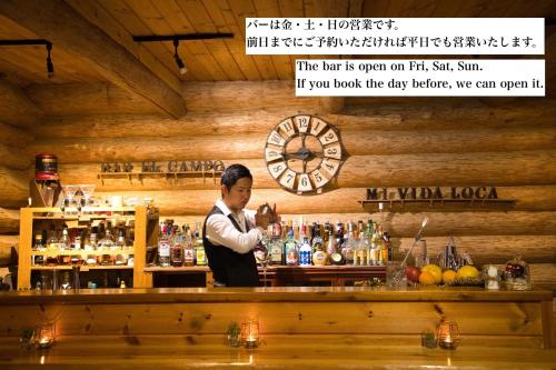 um barman parado atrás de um bar com um relógio em Guesthouse EL CAMPO em Gokase