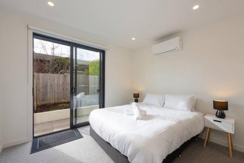 1 dormitorio con cama blanca y ventana grande en Modern 3BR Getaway next to Chadstone, en Oakleigh