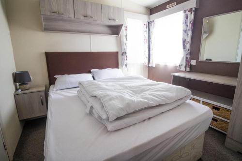 費利克斯托的住宿－6 Berth Caravan With Decking And Wifi At Suffolk Sands Holiday Park Ref 45082c，一间卧室配有一张带白色床单的床和一扇窗户。