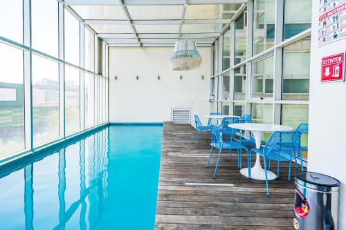 a swimming pool in a building with blue chairs and tables at Increíble departamento en Santa Fe con gym, alberca y estacionamiento in Mexico City