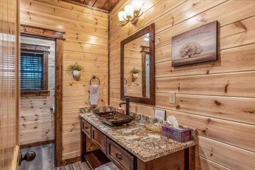 a log cabin bathroom with a sink and a mirror at Large Luxury 2BR Cabin w Hot Tub Double Trouble was designed for fun comfort and memories minutes from buzzling Hochatown and beautiful Beaver Bend State Park in Broken Bow