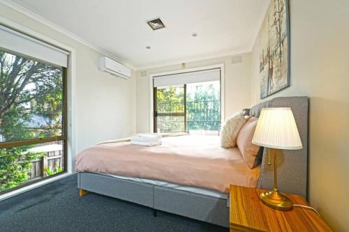 een slaapkamer met een bed met een lamp en een raam bij Maroondah 3BR Brick Entire Home Free Wi-Fi Parking in Ringwood