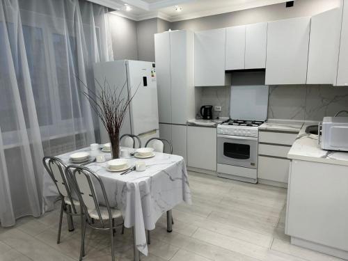 een keuken met een tafel met stoelen en witte apparaten bij 2х комнатная квартира в ЖК Тавангар с евроремонтом in Aqtöbe