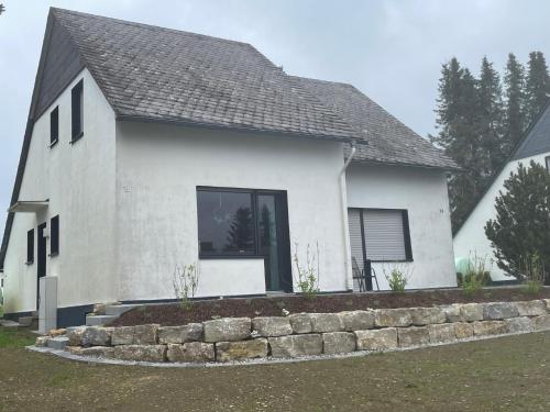 a white house with a stone retaining wall at Ferienhaus Küstelnest in Medebach