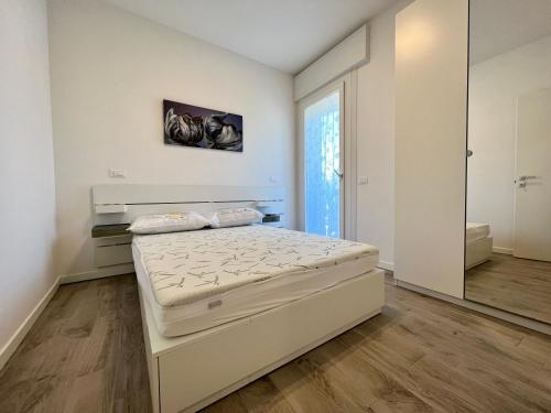 a white bedroom with a bed and a mirror at Condominio Sporting in Lignano Sabbiadoro