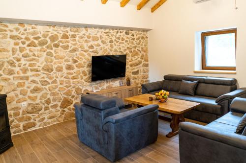 a living room with couches and a tv and a stone wall at Kamena Kuća Vegar in Ljubuški