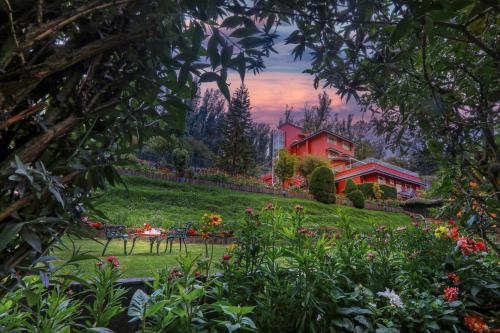 a garden with flowers and a red house in the background at Willow Hill by Nature Resorts and Stays in Ooty