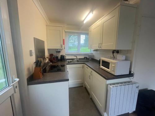 a small kitchen with white cabinets and a microwave at 2 Bedroom Holiday Chalet near Bude in Kilkhampton