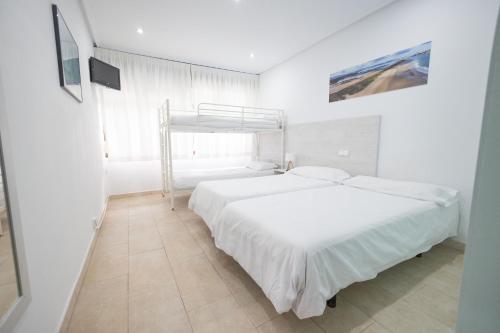 a white bedroom with two beds and a window at Hotel Pinar Somo Surf in Somo