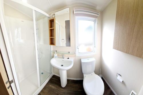 a white bathroom with a toilet and a sink at Caravan With Decking And Free Wifi At Seawick Holiday Park Ref 27214sw in Clacton-on-Sea