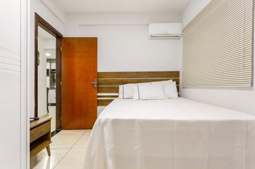 ein Schlafzimmer mit einem weißen Bett und einer Holztür in der Unterkunft Apartamentos Com Suite ,Wi-Fi 500MB , Estacionamento, Elevador, Cozinha Completa , Jr Catito in Brasilia