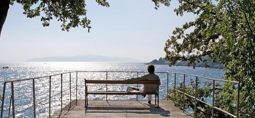 a man sitting on a bench looking at the water at Apartments Villa Bare in Kastav