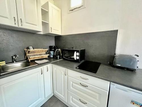 une cuisine avec des armoires blanches, un évier et un micro-ondes dans l'établissement Appartement 2 pièces - PLACE MORNY, à Deauville