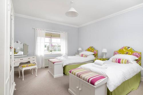 a white bedroom with two beds and a desk at The Cowshed in Laurencekirk