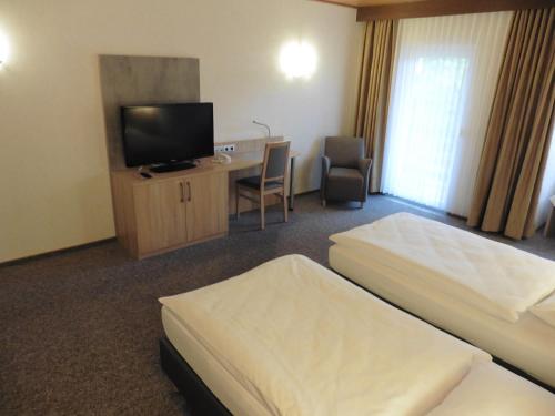 a hotel room with two beds and a desk and a tv at Hotels Landhaus Dieterichs in Wolfsburg