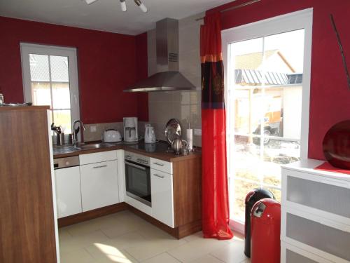 a kitchen with red walls and white cabinets and a window at Ostseelicht in Zierow