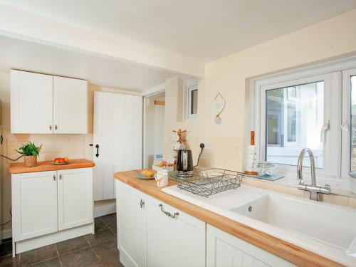 a kitchen with white cabinets and a sink and a window at Otters Cottage in Ottery Saint Mary
