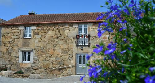 a stone house with a balcony and purple flowers at Casa de Valente - Camariñas in Camariñas