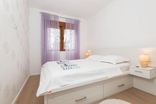 a white bedroom with a large white bed and a window at Cozy one bedroom apartment in Tivat
