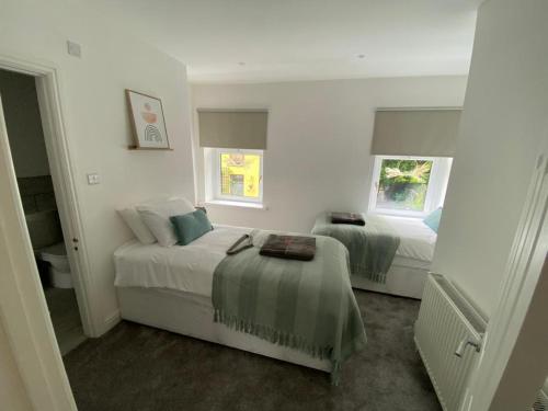 a white bedroom with two beds and two windows at Rhondda Tunnel Cottage by StayStaycations in Treorky