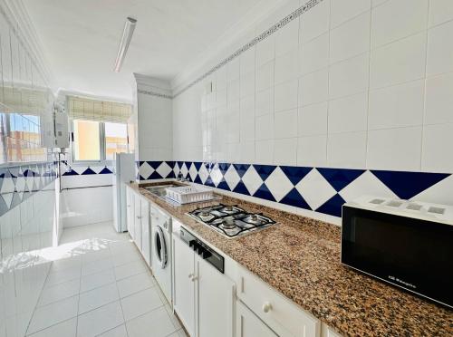 a kitchen with white cabinets and blue and white tiles at Apartamentos Turísticos Santo Rostro in Chipiona