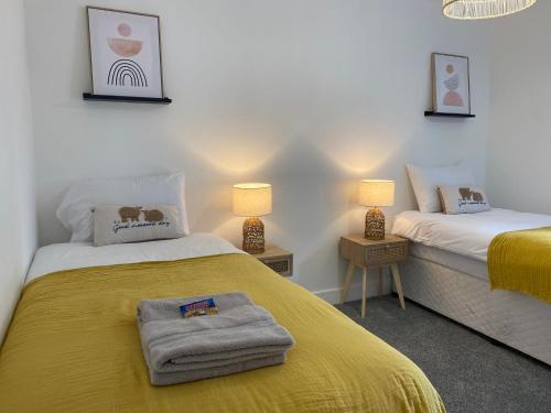 um quarto com 2 camas com lençóis e candeeiros amarelos em Prospect Cottage by StayStaycations em Treorky