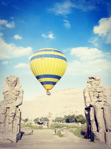 een gele en blauwe luchtballon die over de woestijn vliegt bij Karnak flat in Luxor