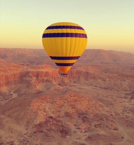 een gele en blauwe ballon die over de woestijn vliegt bij Karnak flat in Luxor