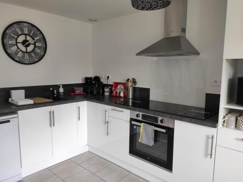 a kitchen with white cabinets and a clock on the wall at Le Petit Gite de la Roseraie in Quiberville
