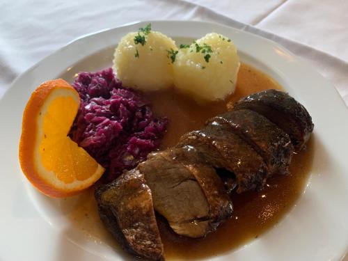 a plate of food with meat and potatoes and an orange slice at Landgasthof Zum Ring in Ringleben